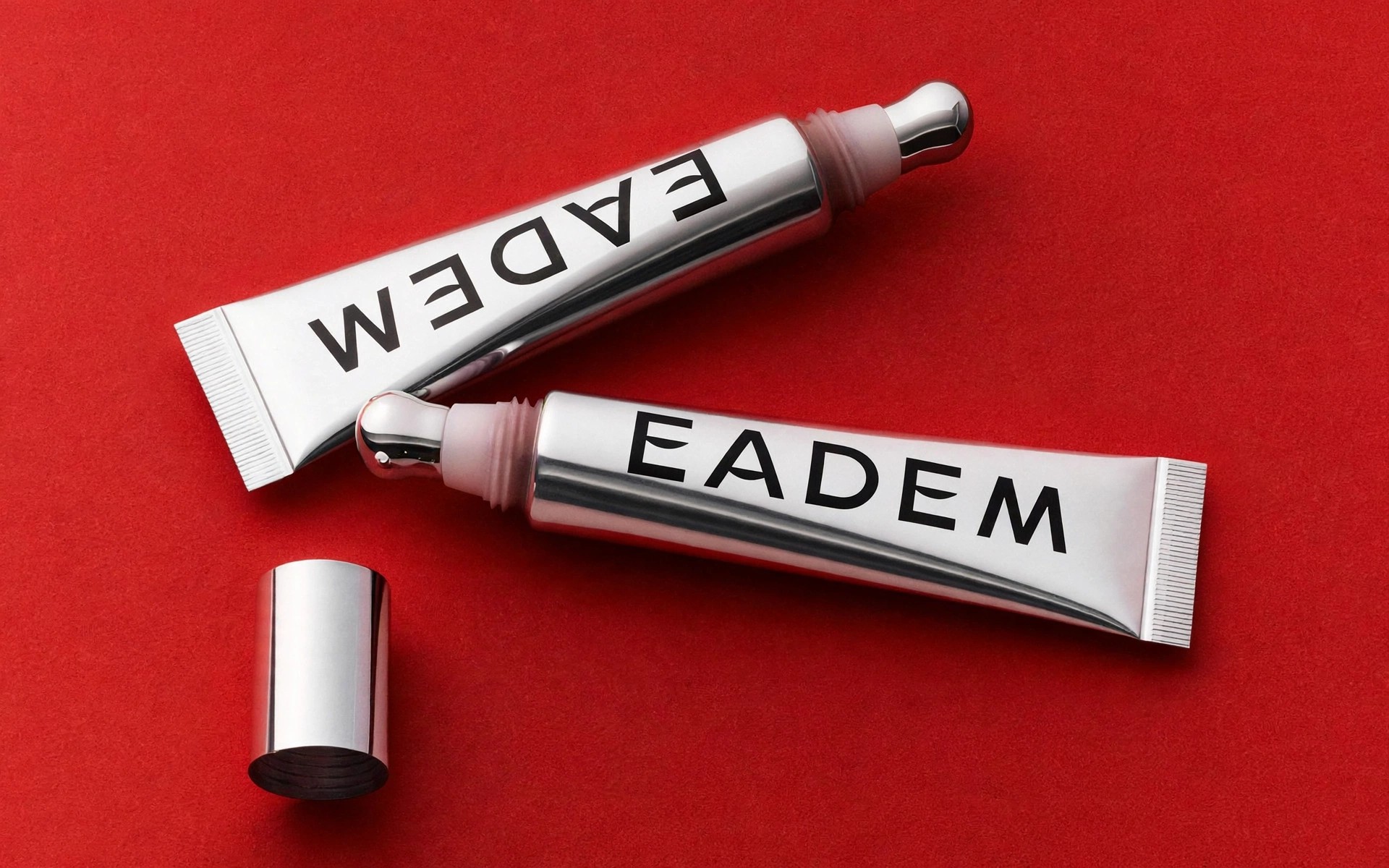 Silver Eadem tubes lie on solid red surface.