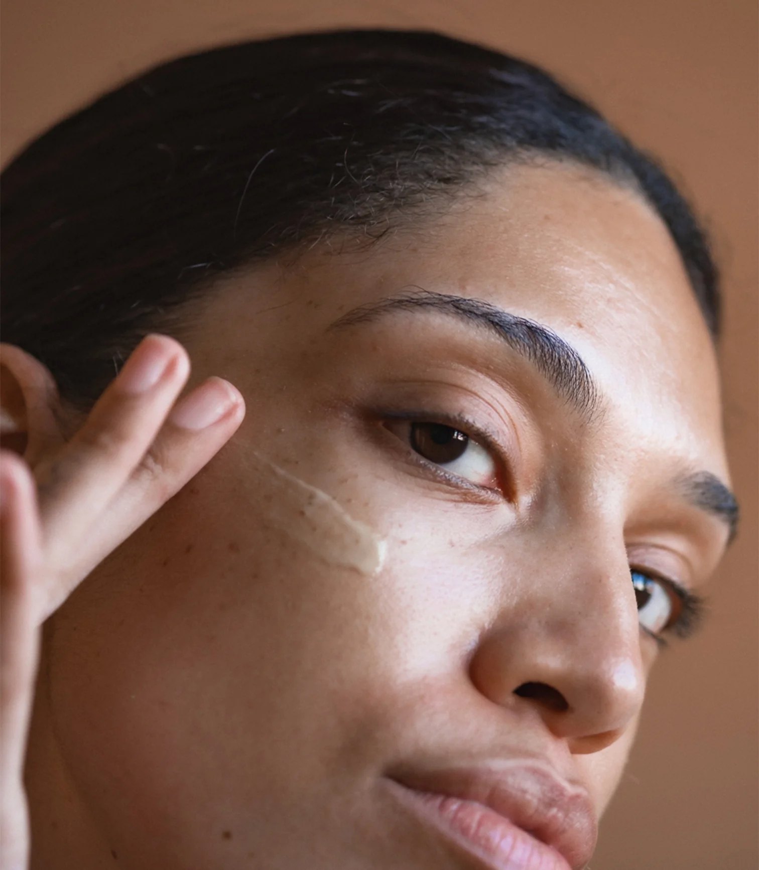 Cream smoothed beside the eye with fingertips in closeup.