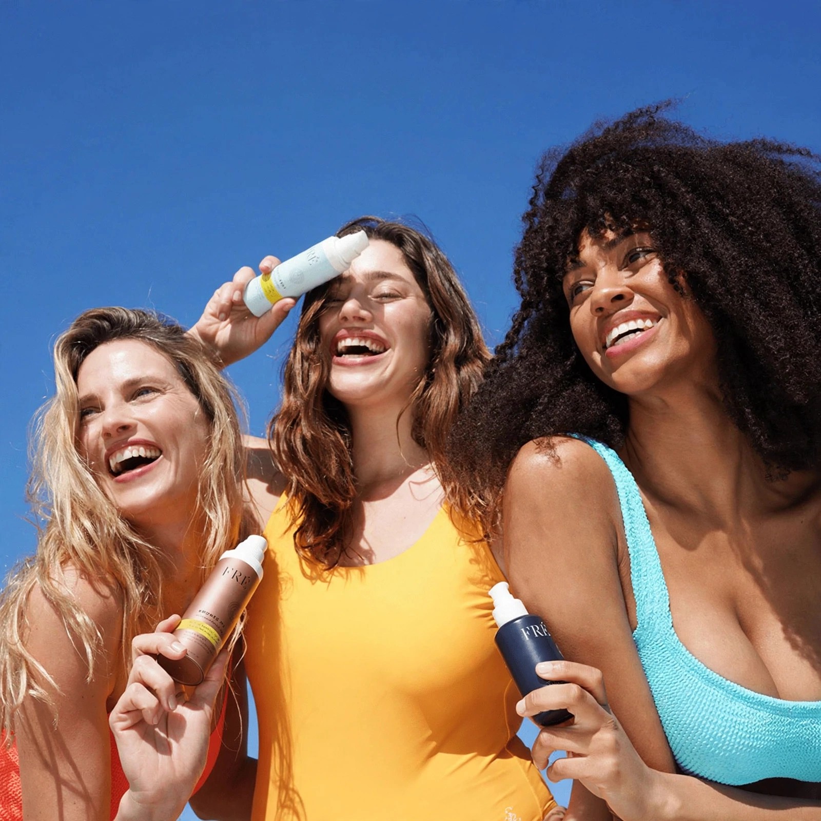 Three laughing women holding Fre bottles in sunlight.