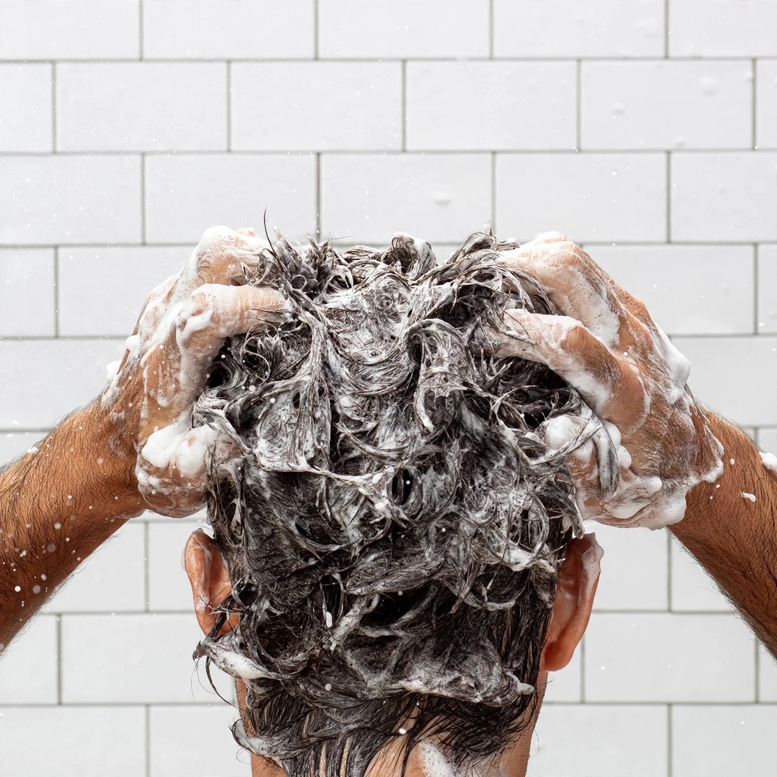 Hands massaging foamy lather into wet hair in shower.