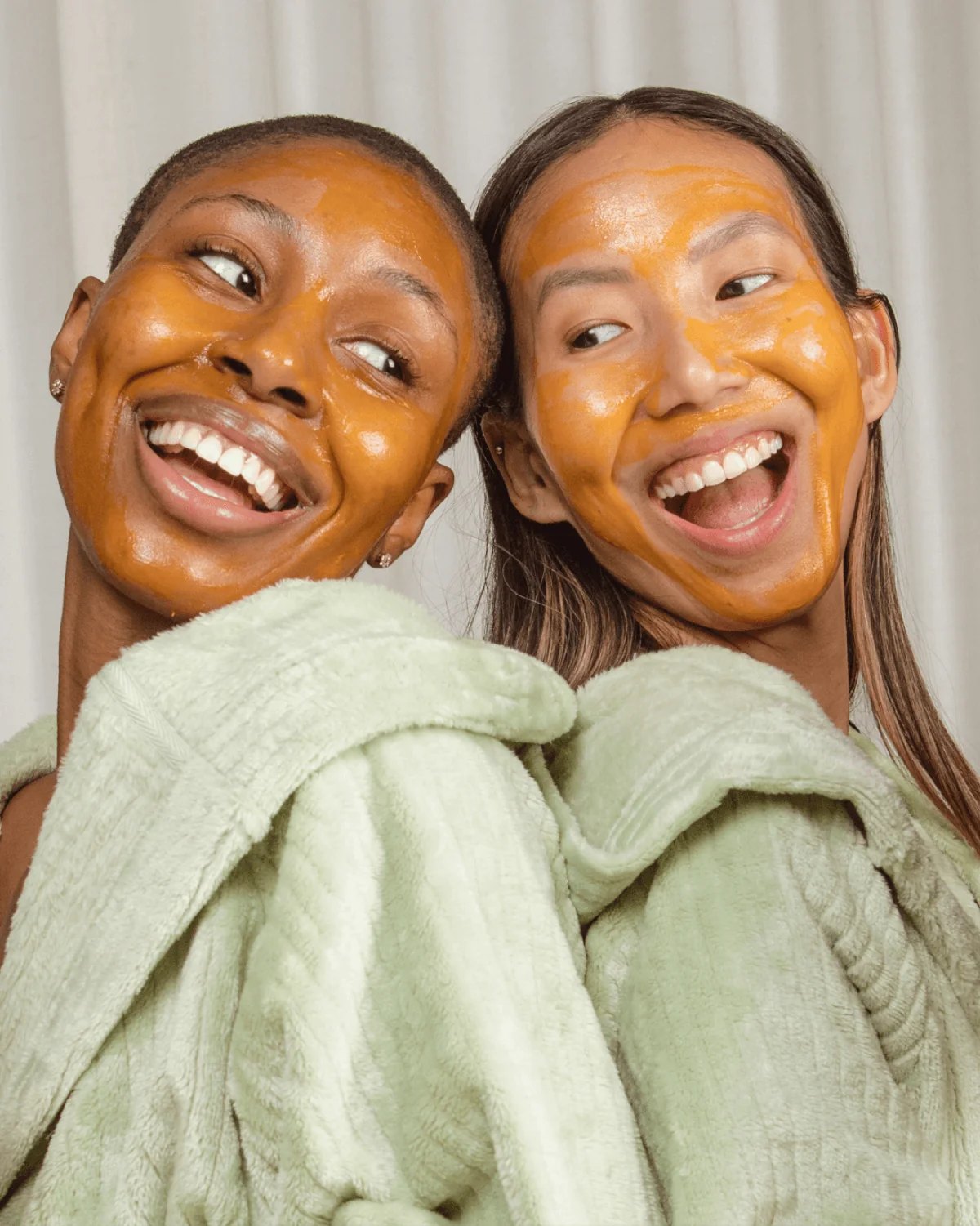Two smiling women in robes wear orange Hyper mask.