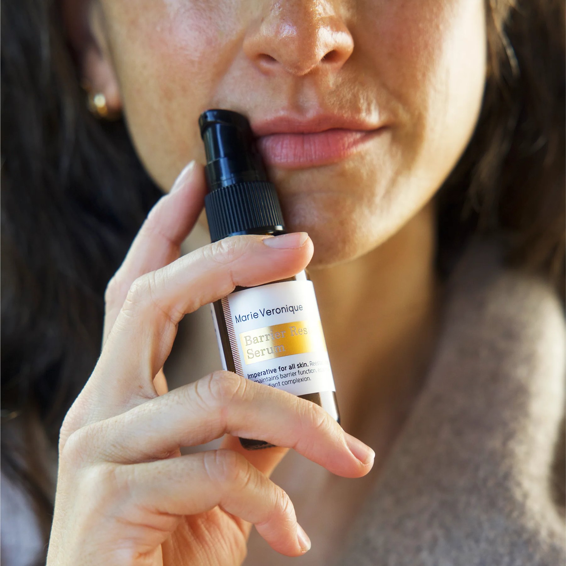 A woman holds the Barrier Restore Serum bottle near her chin.