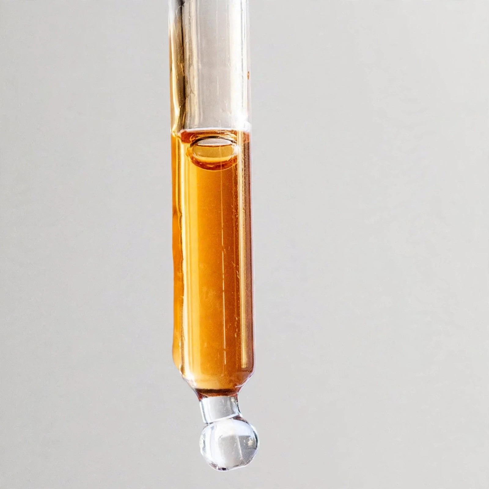 Golden facial oil dripping from a clear glass dropper.