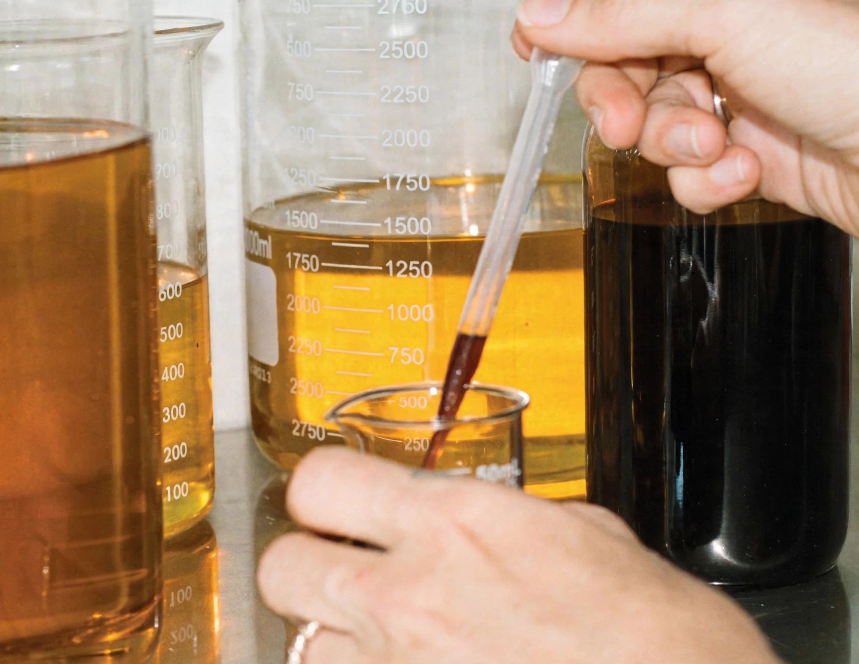 Hands blending botanical oils with pipette and glass beakers.