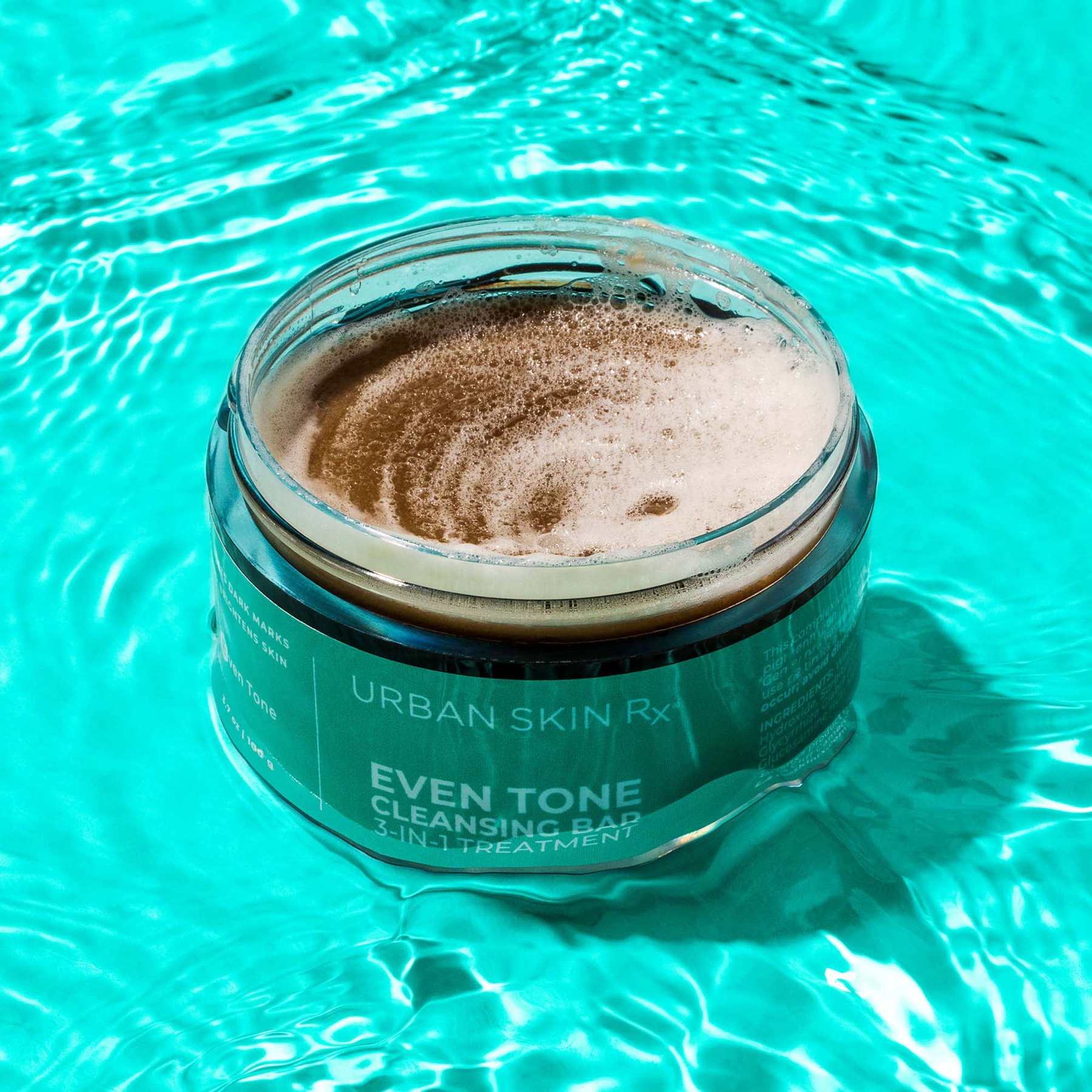 Open Even Tone Cleansing Bar jar with foam surrounded by blue water.