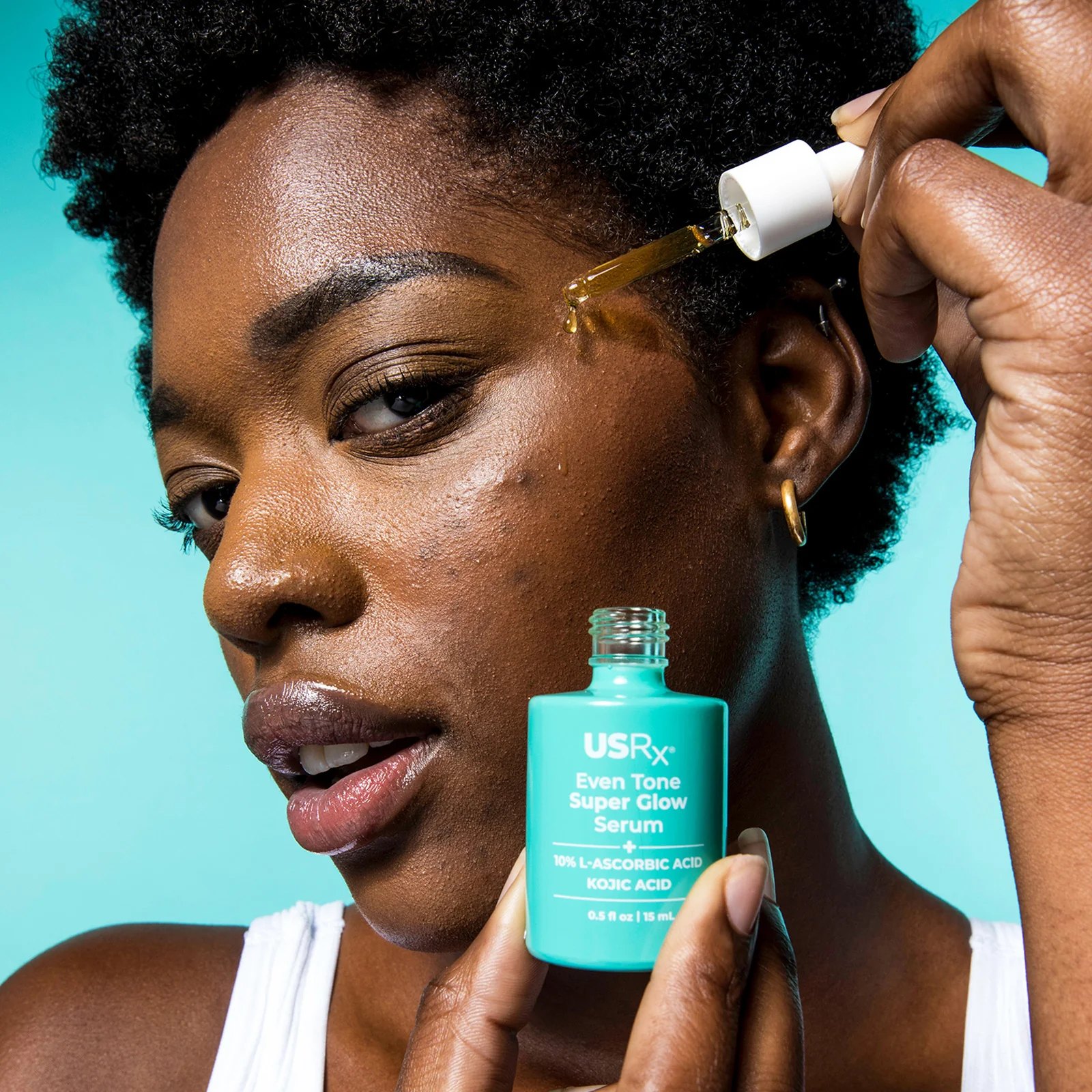 Woman applying Even Tone Super Glow Serum dropper near her cheek.